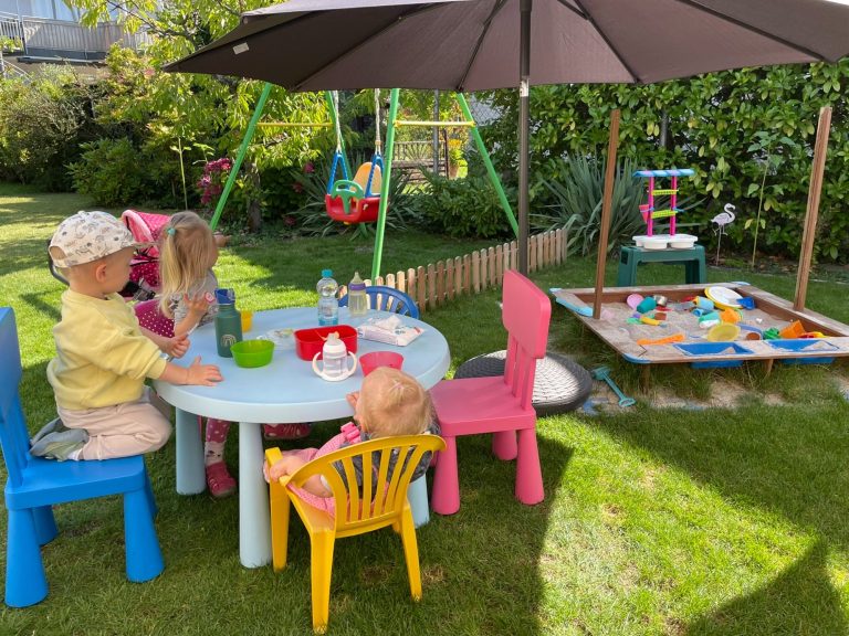 Kinder spielen im Garten mit Spielzeug und einem Hula-Hoop-Reifen.